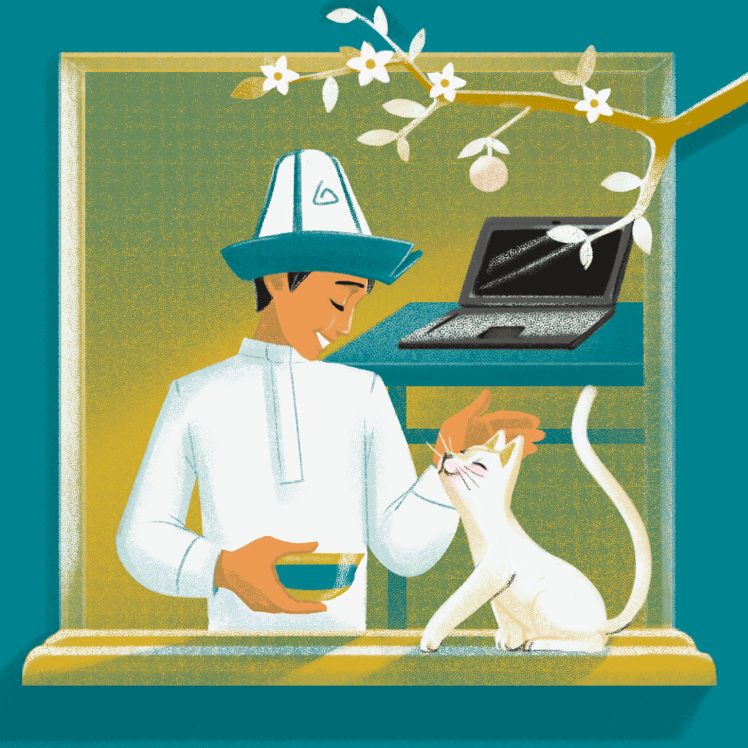 A young man in traditional Kyrgyz clothes feeds and pets a white cat. His computer is in the background.